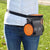 A woman wearing the Wolf in Winter Dog treat training pouch with an orange neoprene top, she has it around her waist, and an orange silicone collapsible pet bowl hooked on the side.